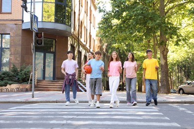 Photo of Group of happy teenage friends crossing road together outdoors