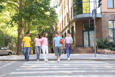 Photo of Group of happy teenage friends crossing road together outdoors