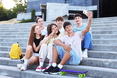 Photo of Group of happy teenage friends taking selfie on steps outdoors