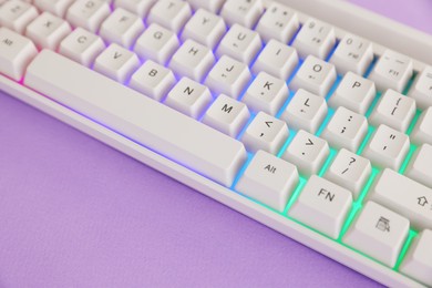 Photo of Modern computer keyboard with RGB lighting on violet background, closeup