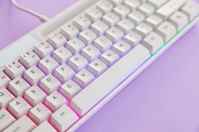 Photo of Modern computer keyboard with RGB lighting on violet background, closeup