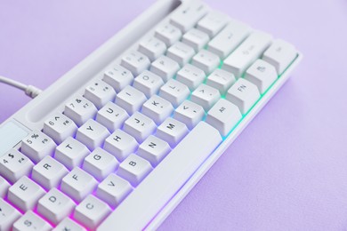 Photo of Modern computer keyboard with RGB lighting on violet background, closeup