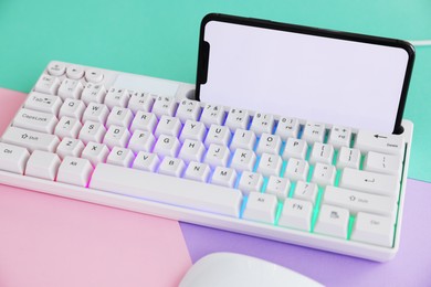 Photo of Modern keyboard with RGB lighting and smartphone on color background, closeup
