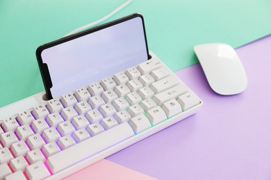 Photo of Modern keyboard with RGB lighting, smartphone and computer mouse on color background, closeup