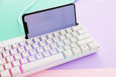 Photo of Modern computer keyboard with RGB lighting and smartphone on color background, closeup