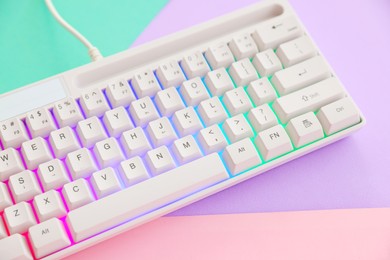 Photo of Modern computer keyboard with RGB lighting on color background, above view