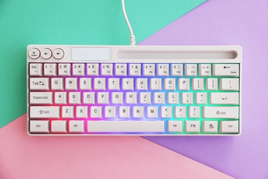 Photo of Modern computer keyboard with RGB lighting on color background, top view