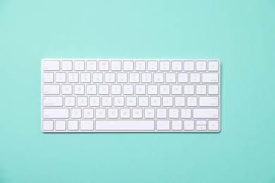 Photo of Modern wireless computer keyboard on turquoise background, top view