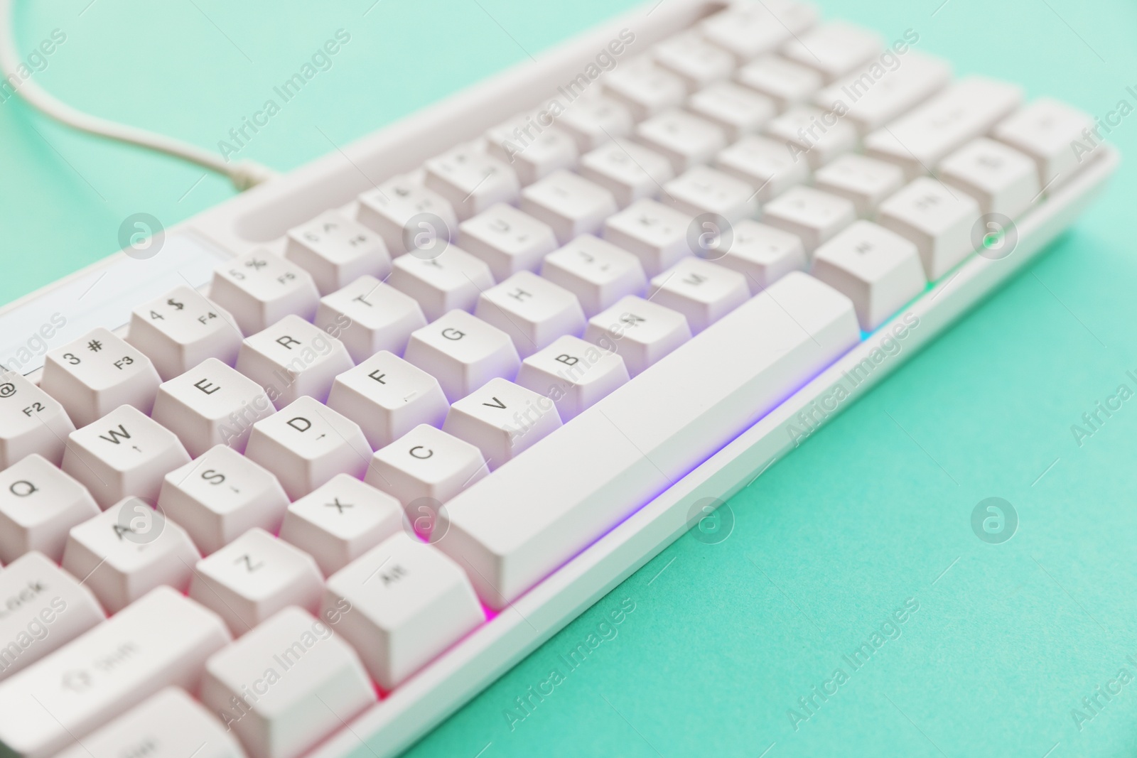 Photo of Modern computer keyboard with RGB lighting on turquoise background, closeup