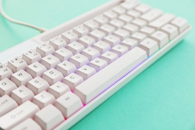 Photo of Modern computer keyboard with RGB lighting on turquoise background, closeup