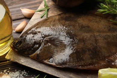 Photo of Fresh flounder fish, salt and rosemary on wooden table, closeup. Raw seafood