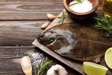 Photo of Fresh flounder fish, salt and products on wooden table, closeup. Raw seafood