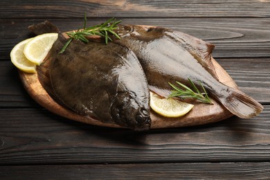 Photo of Fresh flounder fish, lemon and rosemary on wooden table, closeup. Raw seafood