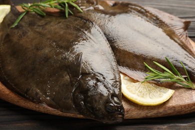 Photo of Fresh flounder fish, lemon and rosemary on wooden table, closeup. Raw seafood