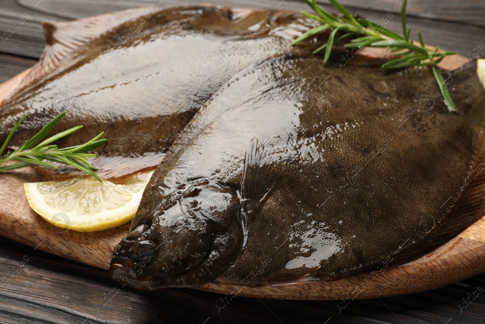 Photo of Fresh flounder fish, lemon and rosemary on wooden table, closeup. Raw seafood