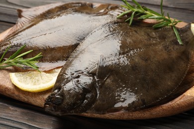 Photo of Fresh flounder fish, lemon and rosemary on wooden table, closeup. Raw seafood