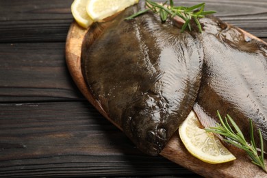 Photo of Fresh flounder fish, lemon and rosemary on wooden table, closeup. Raw seafood
