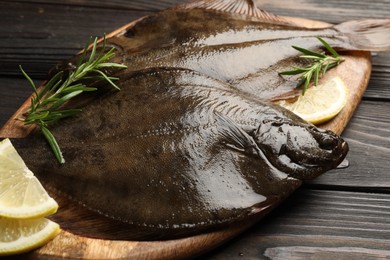 Photo of Fresh flounder fish, lemon and rosemary on wooden table, closeup. Raw seafood
