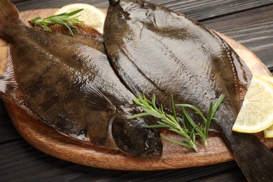 Photo of Fresh flounder fish, lemon and rosemary on wooden table, closeup. Raw seafood