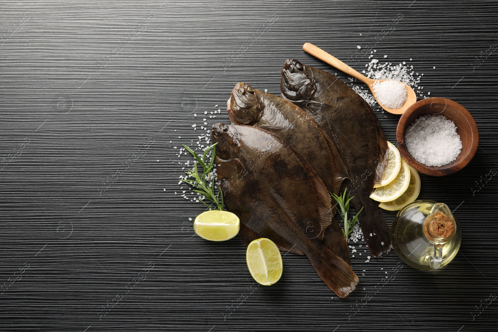 Photo of Fresh flounder fish, salt and products on black wooden table, flat lay with space for text. Raw seafood