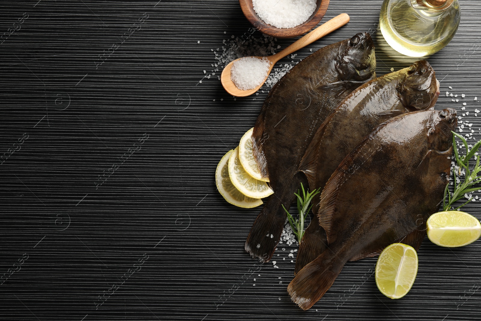 Photo of Fresh flounder fish, salt and products on black wooden table, flat lay with space for text. Raw seafood