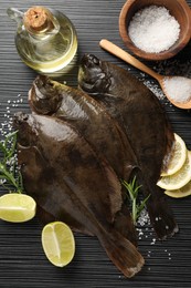 Photo of Fresh flounder fish, salt and products on black wooden table, flat lay. Raw seafood