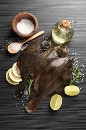 Photo of Fresh flounder fish, salt and products on black wooden table, flat lay. Raw seafood