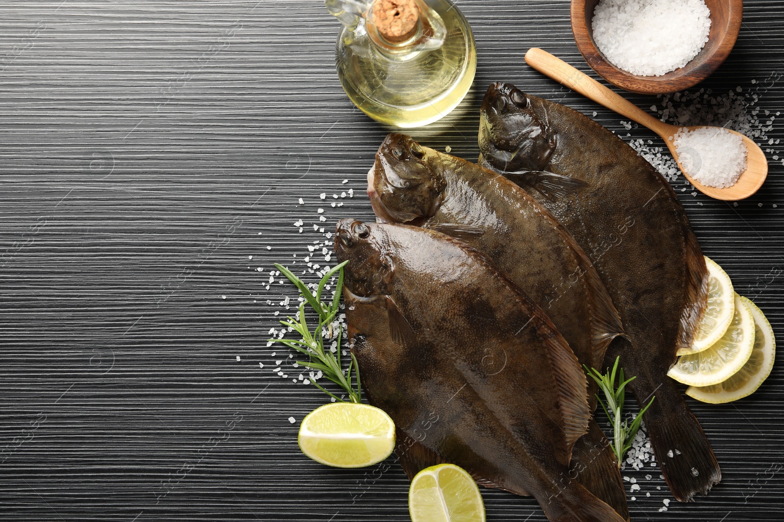 Photo of Fresh flounder fish, salt and products on black wooden table, flat lay with space for text. Raw seafood