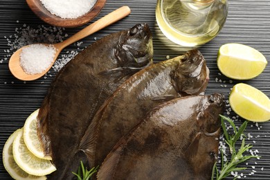 Photo of Fresh flounder fish, salt and products on black wooden table, flat lay. Raw seafood