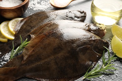 Photo of Fresh flounder fish, salt and products on black wooden table, closeup. Raw seafood