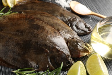 Photo of Fresh flounder fish, salt and products on black wooden table, closeup. Raw seafood