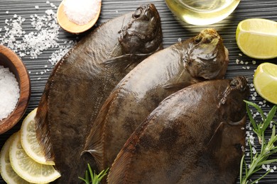 Photo of Fresh flounder fish, salt and products on black wooden table, flat lay. Raw seafood