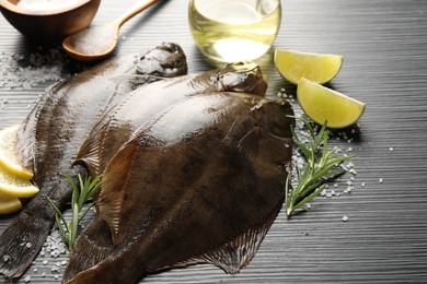Photo of Fresh flounder fish, salt and products on black wooden table, closeup. Raw seafood