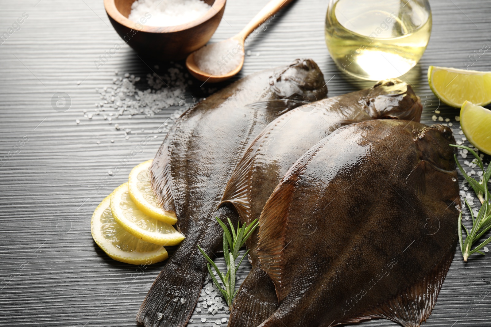 Photo of Fresh flounder fish, salt and products on black wooden table, closeup. Raw seafood