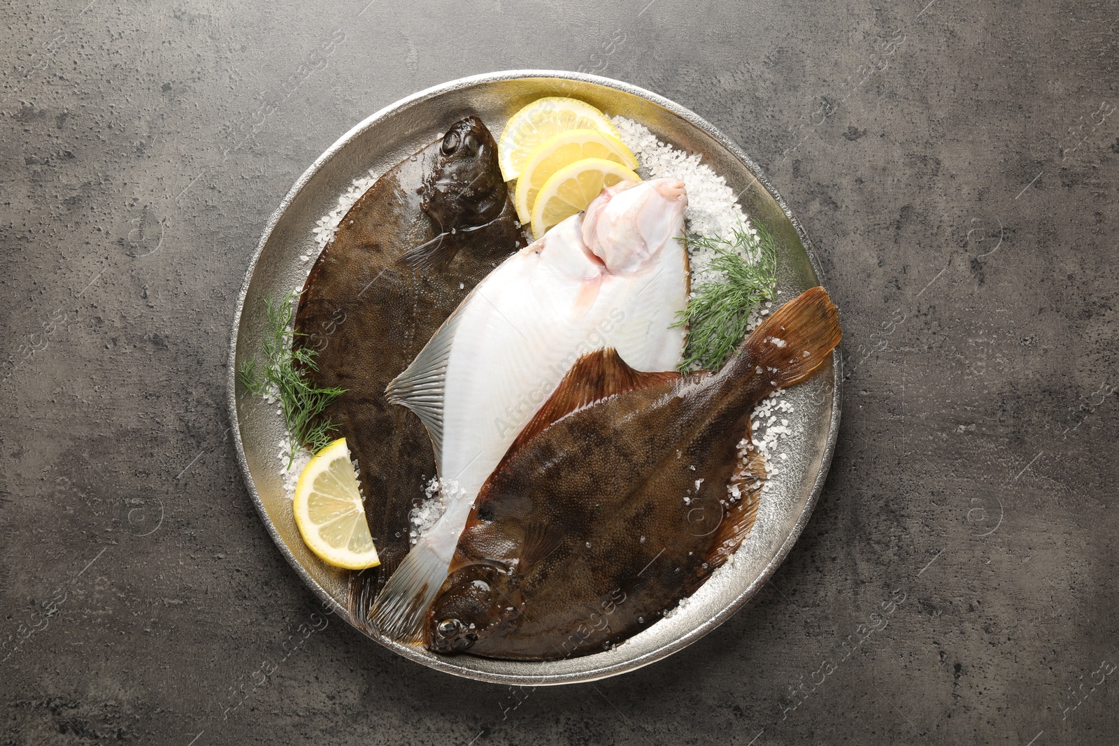 Photo of Fresh flounder fish, salt, lemon and dill on grey textured table, top view. Raw seafood