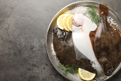 Photo of Fresh flounder fish, salt, lemon and dill on grey textured table, top view with space for text. Raw seafood