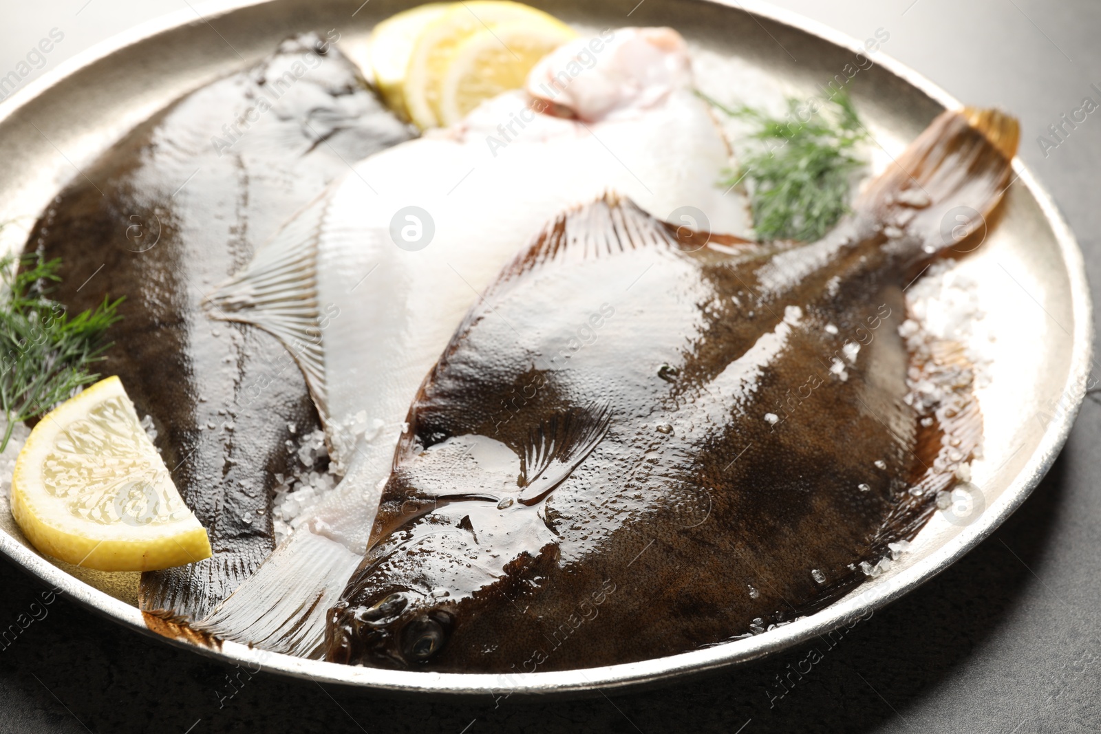 Photo of Fresh flounder fish, salt, lemon and dill on grey textured table, closeup. Raw seafood