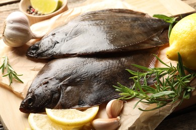Photo of Fresh flounder fish, lemon, rosemary and garlic on wooden table, closeup. Raw seafood