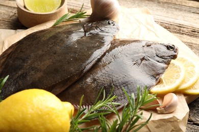 Photo of Fresh flounder fish, lemon, rosemary and garlic on wooden table, closeup. Raw seafood