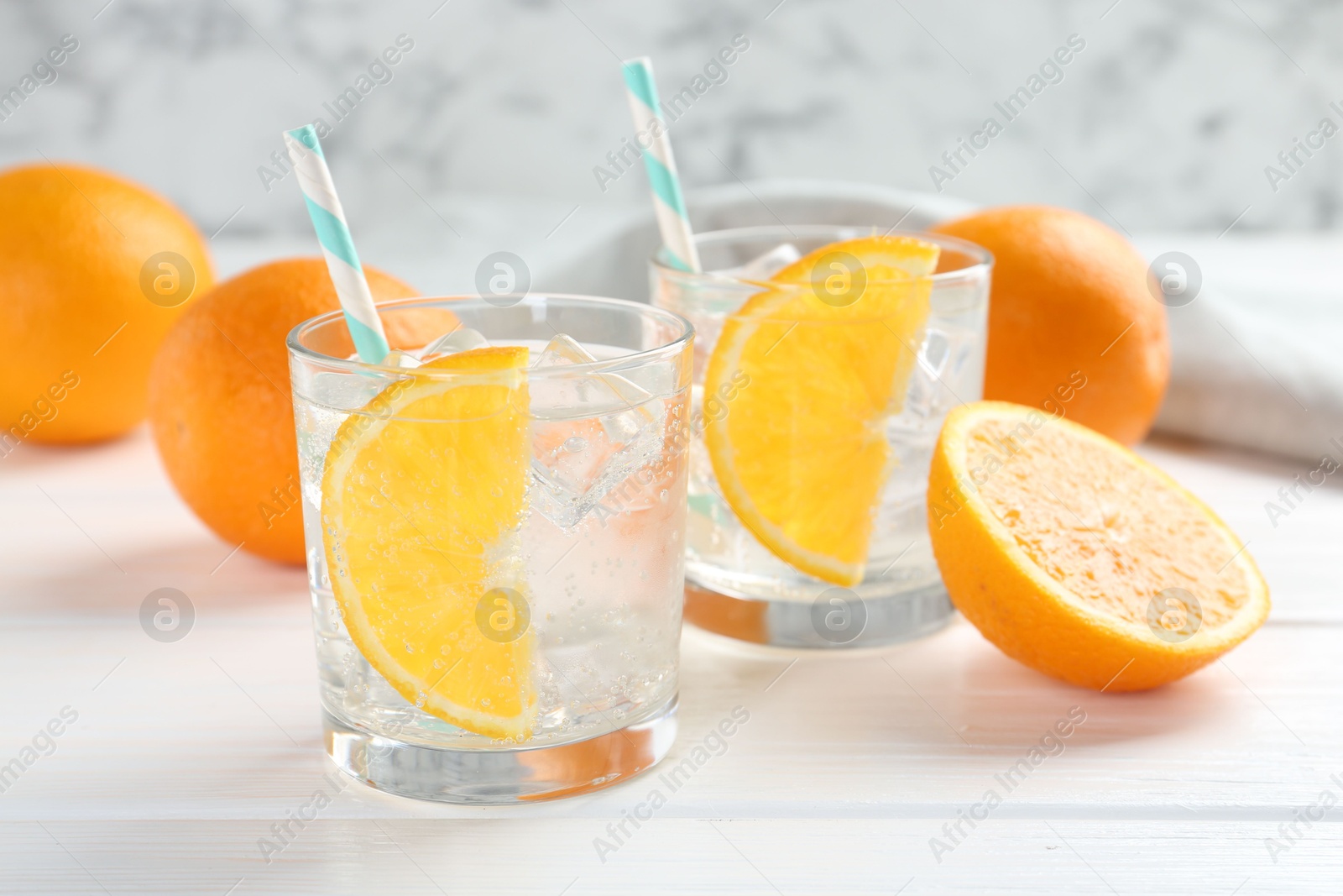 Photo of Sparkling water with orange slices in glasses and fresh fruits on white wooden table, closeup