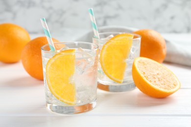 Photo of Sparkling water with orange slices in glasses and fresh fruits on white wooden table, closeup