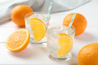 Photo of Sparkling water with orange slices in glasses and fresh fruits on white wooden table, closeup