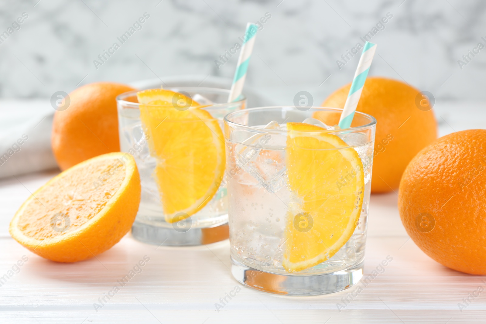 Photo of Sparkling water with orange slices in glasses and fresh fruits on white wooden table, closeup