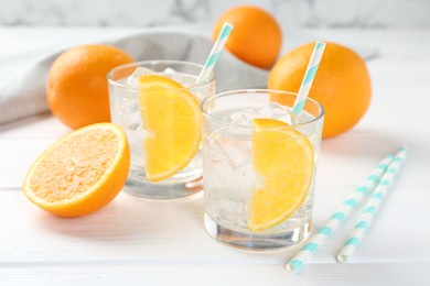 Photo of Sparkling water with orange slices in glasses and fresh fruits on white wooden table, closeup