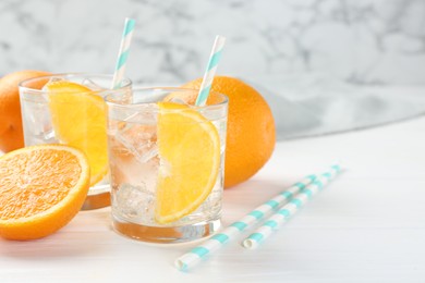 Photo of Sparkling water with orange slices in glasses and fresh fruits on white wooden table, closeup. Space for text