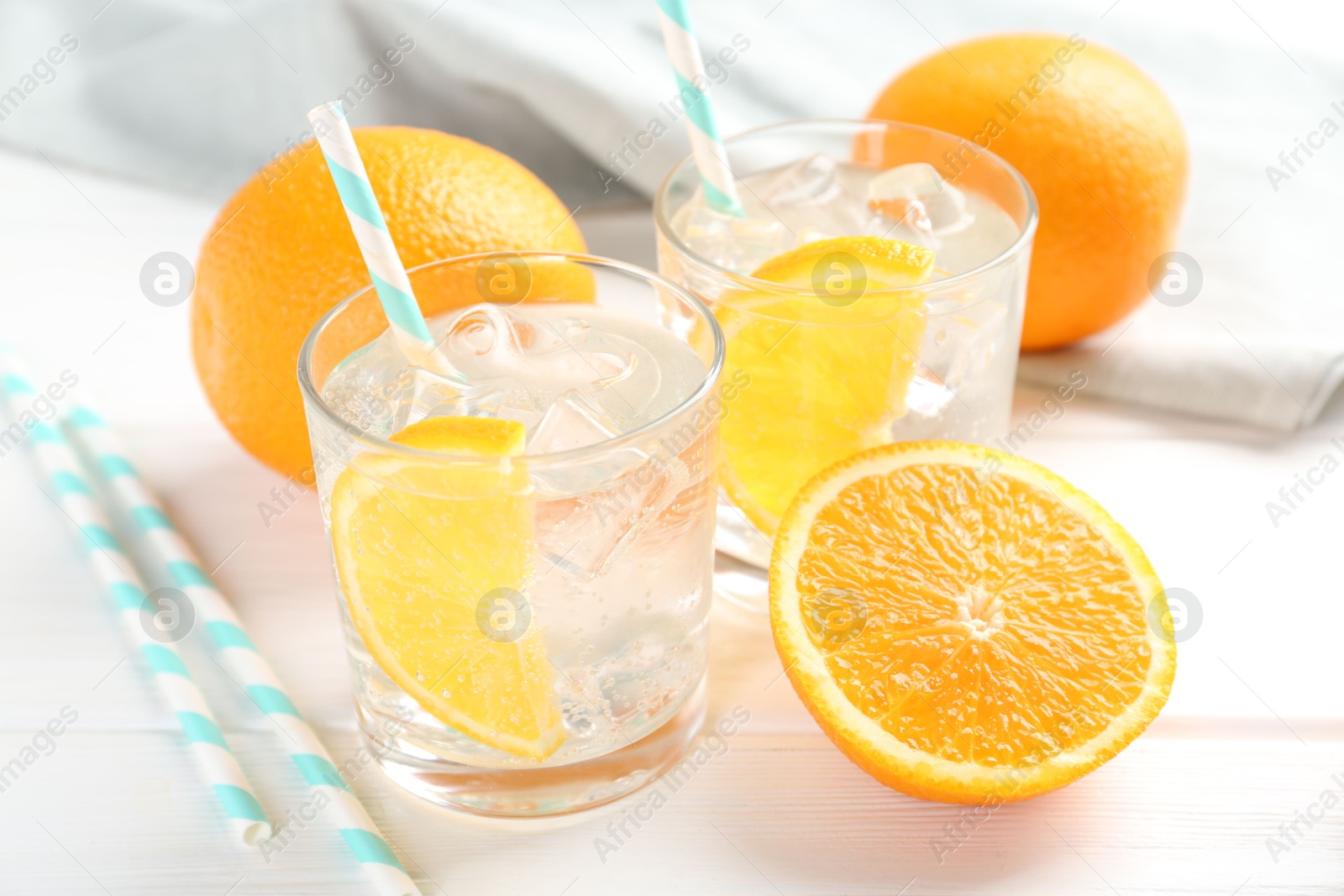 Photo of Sparkling water with orange slices in glasses and fresh fruits on white wooden table, closeup