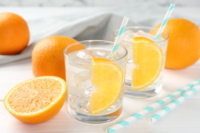 Photo of Sparkling water with orange slices in glasses and fresh fruits on white wooden table, closeup