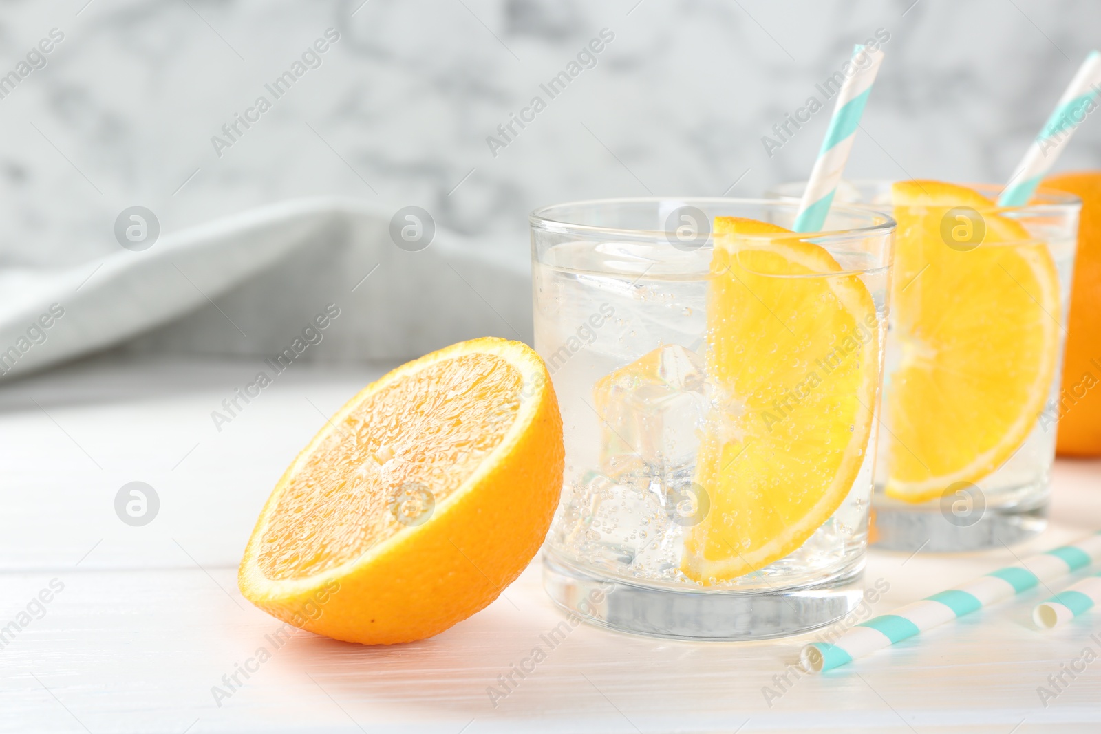 Photo of Sparkling water with orange slices in glasses and fresh fruit on white wooden table, closeup