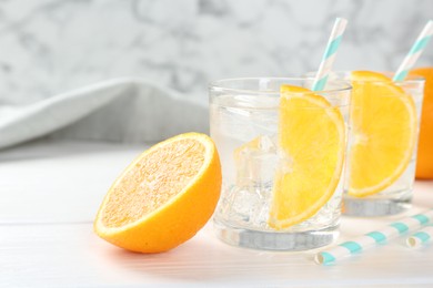 Photo of Sparkling water with orange slices in glasses and fresh fruit on white wooden table, closeup