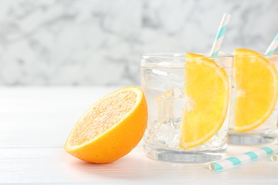 Photo of Sparkling water with orange slices in glasses and fresh fruit on white wooden table, closeup. Space for text